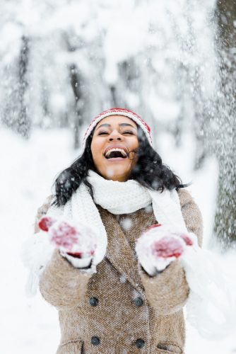 Attractive African American woman throwing snow and smiling in winter forest