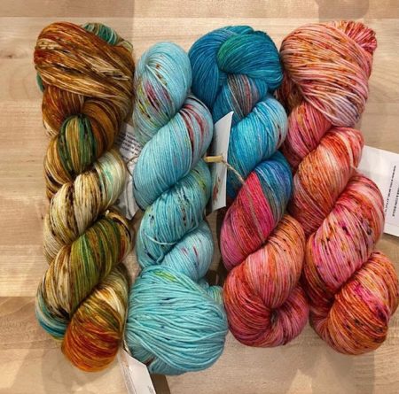 Four skeins of yarn in varying shades of gold, coral, pink, light blue and teal.