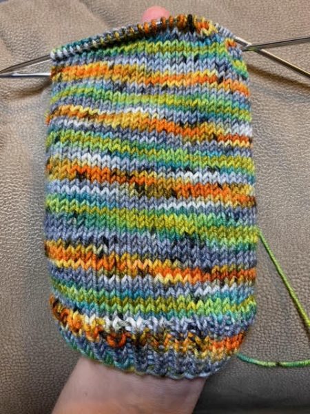The cuff of a sock in orange, green, gray and white with black speckles