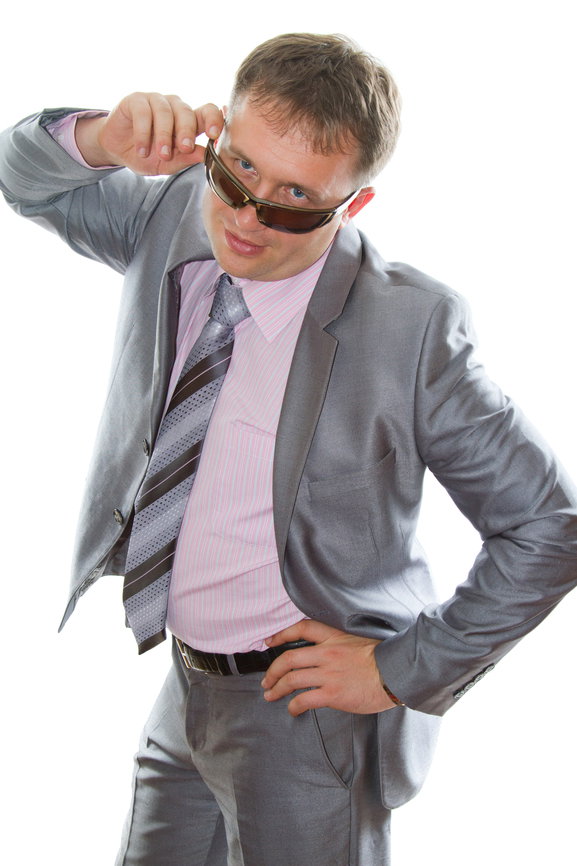 Sleazy business man with grey suit dipping his sunglasses with one hand on his hip.