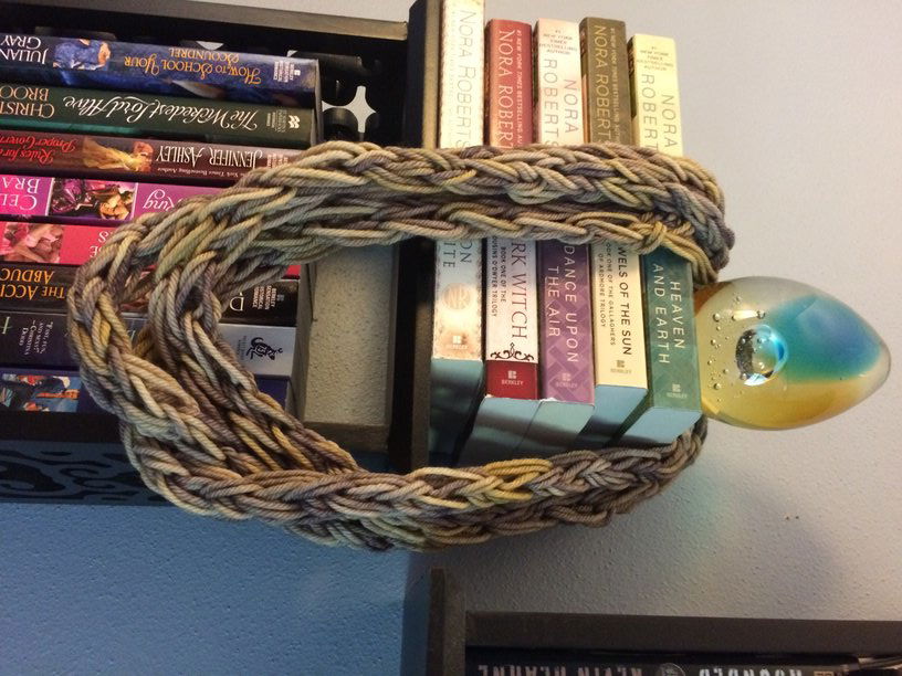 A braided loop of three fingerknit strands in a three-strand necklace of sorts, draped over a paperweight on top of some books.