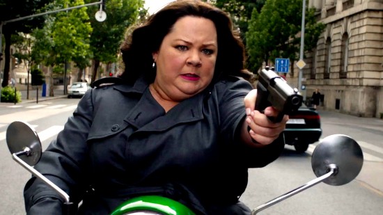 McCarthy, on a vespa, aiming a gun with a Don't fuck with me expression.