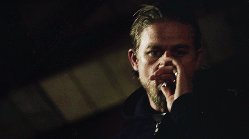 Charlie Hunnam in dark surroundings and low light pulling a cigarette out of his mouth in an animated loop - you can only see the contours of his face and the smoke