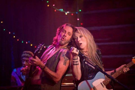 Rick Springfield and Meryl Streep rocking out with big hair and guitars under rose and blue lighting.