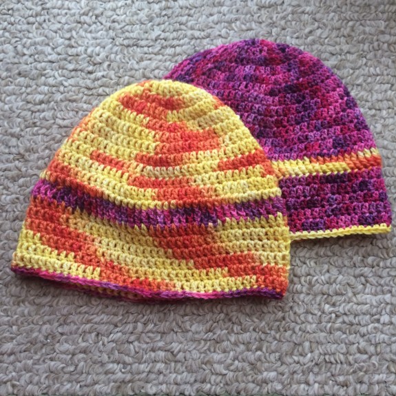 Variegated crochet caps, one in yellow and red, and one in a mix of purple, fuchsia and pink - they're spiffy!