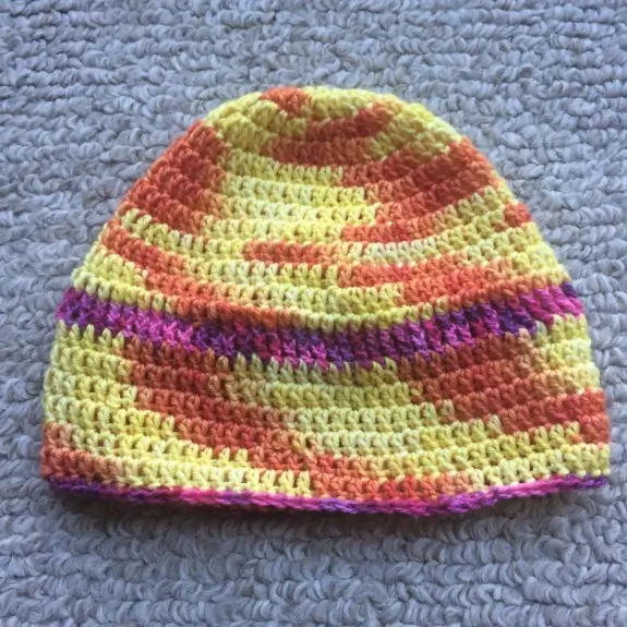 Beanie style crochet cap with red and yellow variegated pattern, almost like a spiral tie die