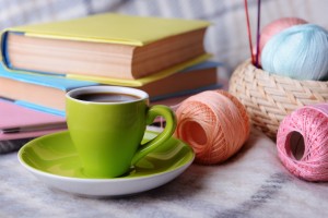 Cup of coffee and yarn for knitting on plaid with books close-up