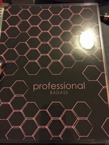 Amandas life planner, which has a pink on brown honeycomb pattern and says PROFESSIONAL BADASS on the front