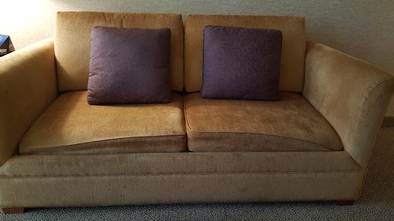 A close up of a very saggy brown couch with purple pillows - the one in my room which was terribly uncomfortable