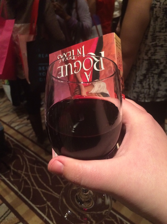 Close up of RedHeadedGirls hand holding a large amount of red wine and a paperback in one hand. 