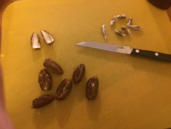 Pitted dates with a knife on a cutting board. RHG sliced the side of the date to remove the pit leaving a pocket in the long edge