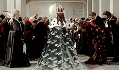 Queen Kristina crowned and wearing royal robes while the court bows around her 