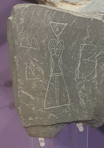 Close up of scratched graffiti on a piece of flat grey slate, a woman with no top on etched in the 9th century
