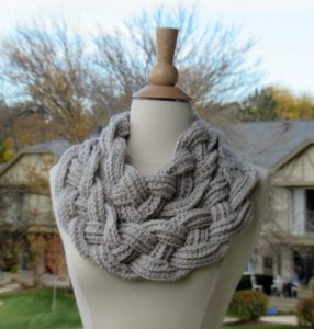 Braided cowl in grey with two looping fat braids over the neck of a mannequin form