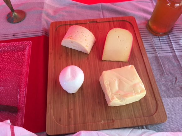 Cheese board with four cheeses - three that are light yellow, two with small holes, and one round white cheese that looks really good 