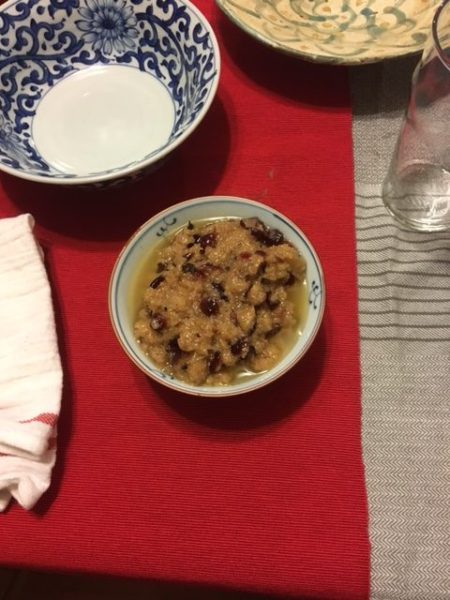 The finished sauce, which is orange and dark red from the cranberries on the table with a red cloth behind it.