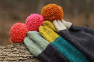 stack of conversationalist hats, with colored pompoms, a short bit of color at the top, then a contrasting color the rest of the way