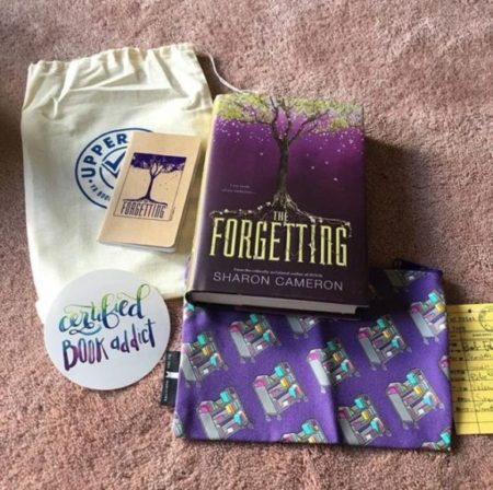 A copy of The Forgetting by Sharon Cameron, a sticker that says Certified book addict, and a pencil bag printed with Library book carts