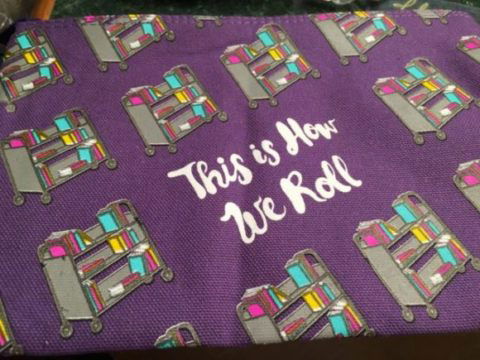 Close up of bag - its purple with library carts on it, and ti reads This Is How We Roll