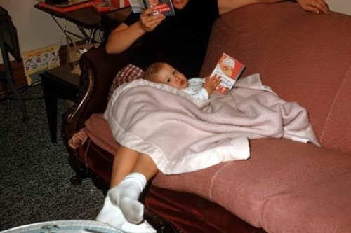 An adorable baby holding an upside down romance novel while snuggling with mom