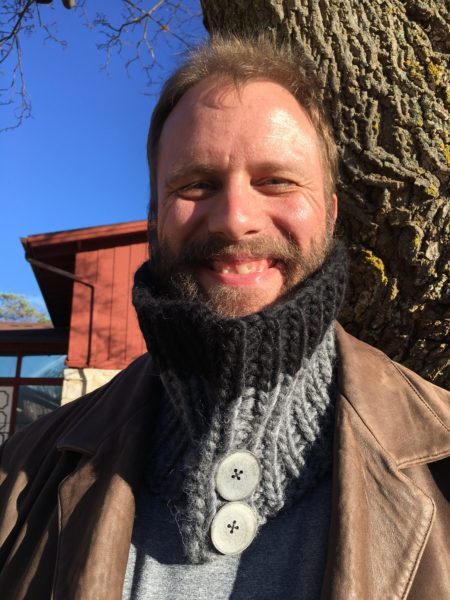 Rich is standing in front of a tree, wearing his cowl buttoned up