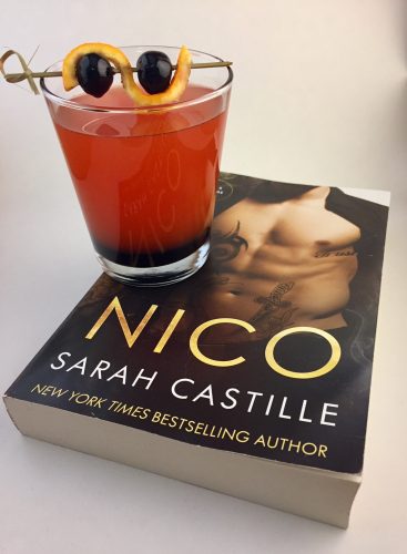 A bright orange Aperol spritz in a high ball glass next to a copy of Nico by Sarah Castille