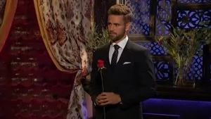 NIck holds a rose, staring vacantly into the middle distance.