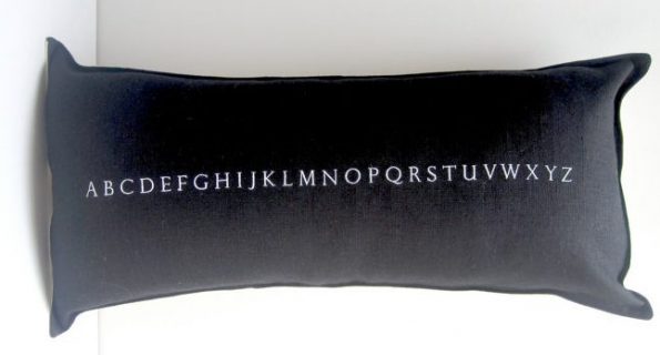 Black linen pillow with the alphabet embroidered on it in white thread 