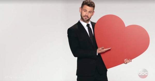 Nick Viall stands holding a big paper heart and looking like kind of a douche.