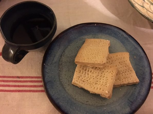 Beige hardtack biscuits on a blue glazed stonewear plate next to a dark mug