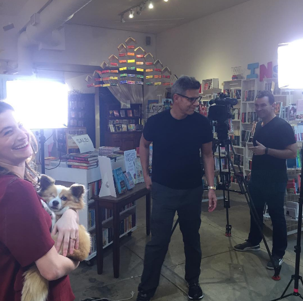 Bea holding Fitzwilliam Waffles in The Ripped BOdice with a camera crew behind her