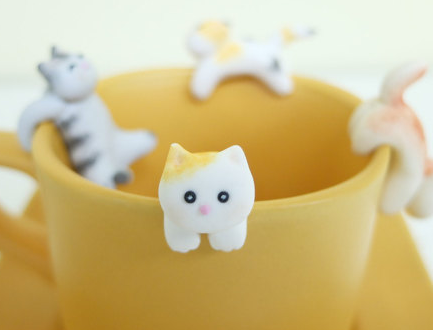 Tiny ceramic cat holding onto teabag 