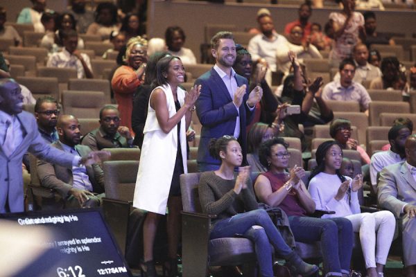 Nick and Rachel stand, applauding, in church.