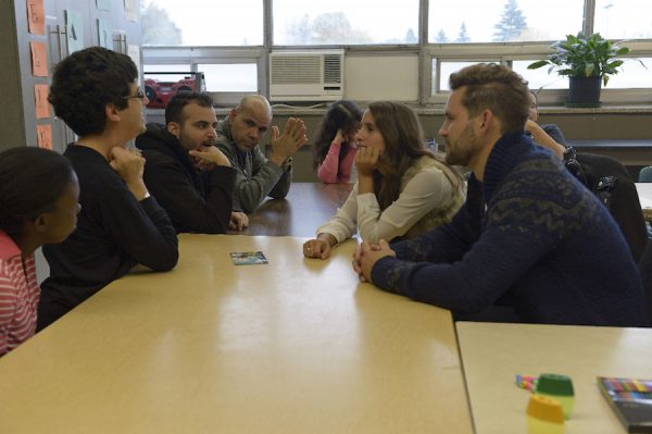 Nick and Vanessa sit across a table from some of her students.