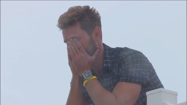 Nick leans over a balcony and sobs, his hands over his face.