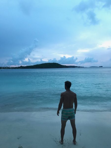 Nick stands on a beach, staring vacantly out toward the ocean.