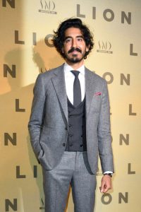 Dev Patel in a grey suit with dark grey double breasted waistcoat and grey tie looking disheveled and handsome