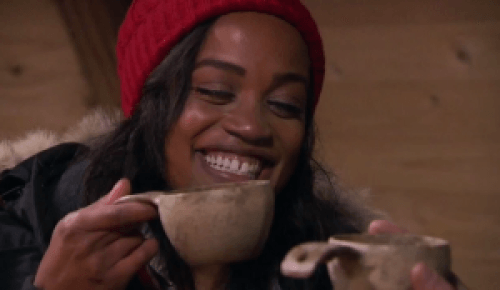 Rachel laughs and drinks out of a mug.