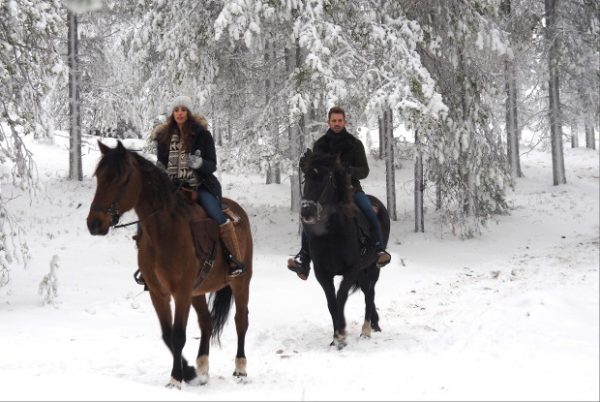 Nick and Vanessa ride horses in a snow covered forest.