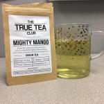 The package of Mighty Mango tea sits next to my glass tea cup which is filled with a light yellow tea. My desk is still sad.