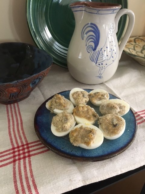 Farced eggs! deviled eggs with raisins on a blue plate with a blue pitcher with a rooster on it behind the plate