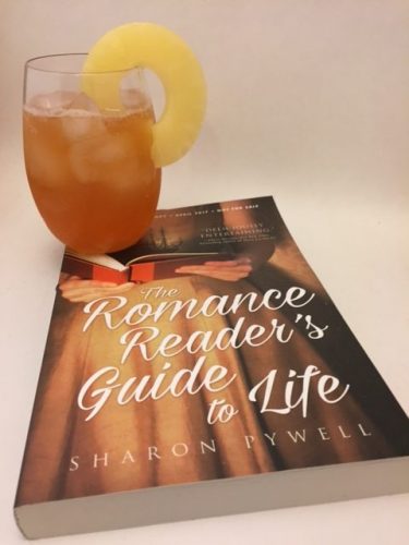 An orange tropical drink garnished with a slice of pineapple, next to a copy of The Romance Reader's Guide to Life by Sharon Pywell