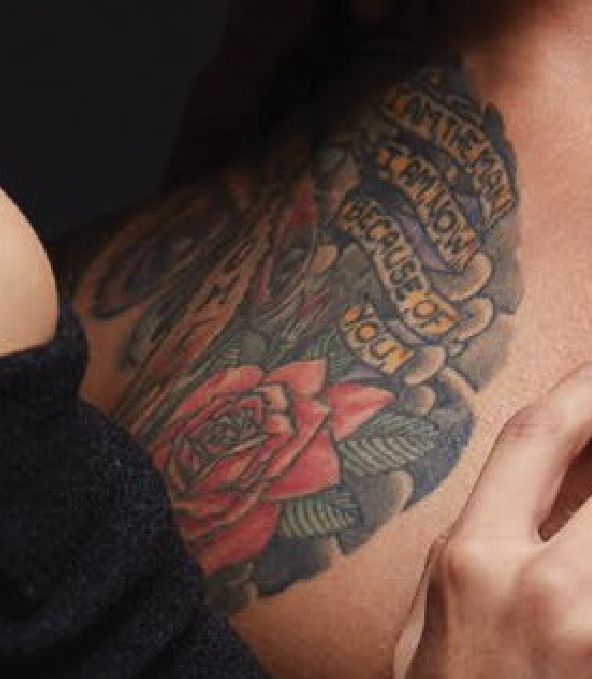 Close up of full color tattoo with a rose and a banner that reads I am the man I am now because of you