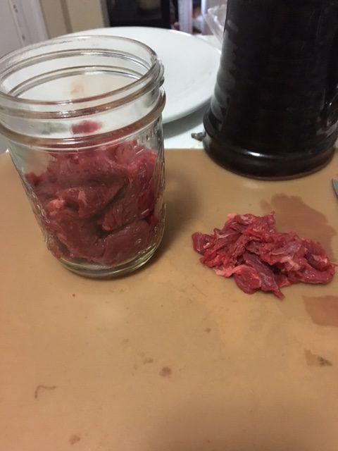 Cleaned beef in a canning jar, with a small pile of connective tissue next to it.