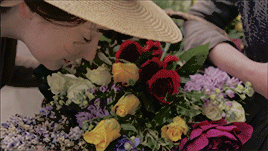 Morwenna, smelling flowers, She has big dark eyes and dark hair, and looks very sweet and kind.