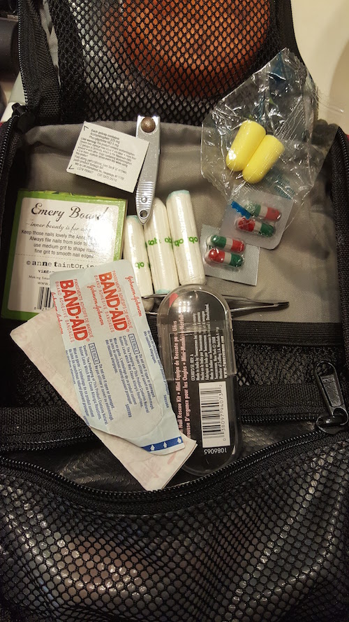 Close up of badnaids, tweezers, tampons, tylenol, ear plugs etc going into zipper pocket