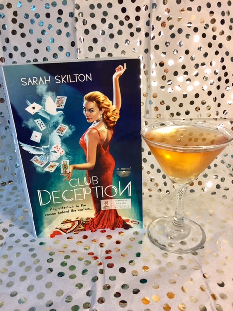 A honey-hued drink in a martini class next to a copy of Club Deception