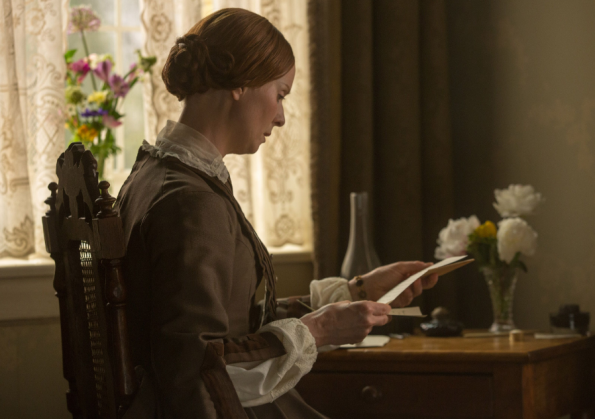 Cynthia Nixon as Emily reading a letter at her desk backlit by a curtain in a dark, drab room