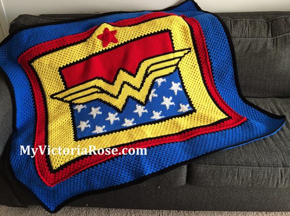 A throw blanket draped across a sofa. The Wonder Woman logo is in the center, with red above and white stars on a blue field below. There are red and blue borders.