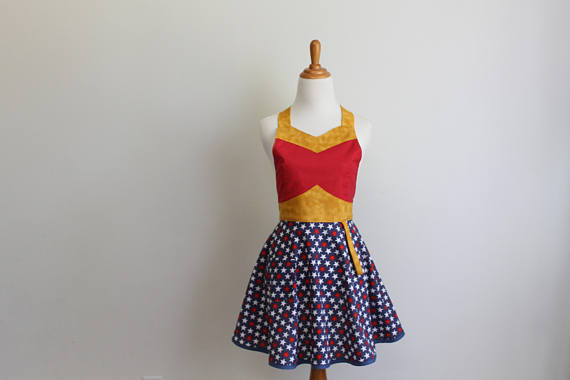 An apron on a dress form. The skirt is blue with stars and the bodice is red. There is gold trim along the bust and waist.